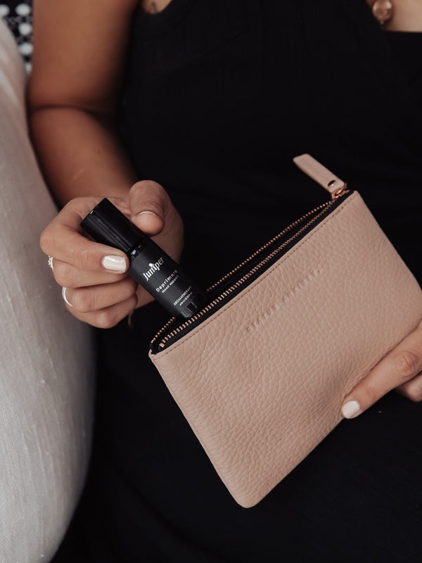 Juniper Deprimere 10ml aromatherapy roller, included in the Cognitive Support + Wellbeing Collection, held beside an open pink handbag.