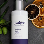 Juniper Intensive Body Lotion 250ml bottle styled on dark stone with olive branches and dried citrus slices.
