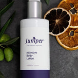 Juniper Intensive Body Lotion 250ml bottle styled on dark stone with olive branches and dried citrus slices.