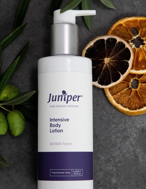 Juniper Intensive Body Lotion 250ml bottle styled on dark stone with olive branches and dried citrus slices.