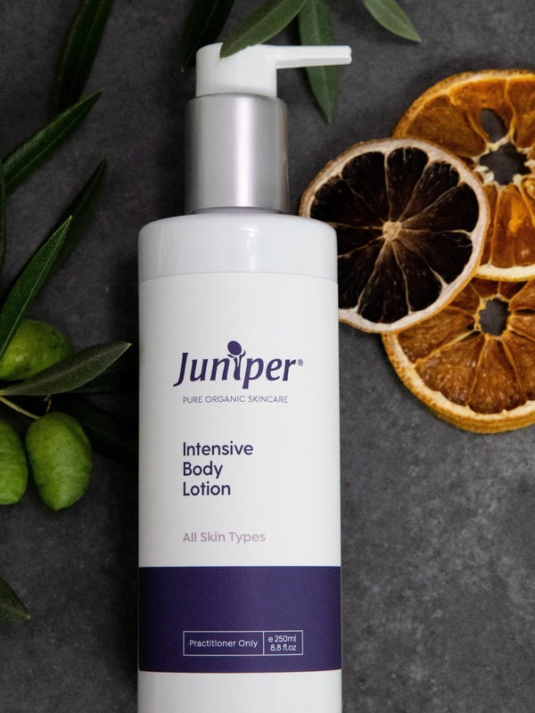 Juniper Intensive Body Lotion 250ml bottle styled on dark stone with olive branches and dried citrus slices.