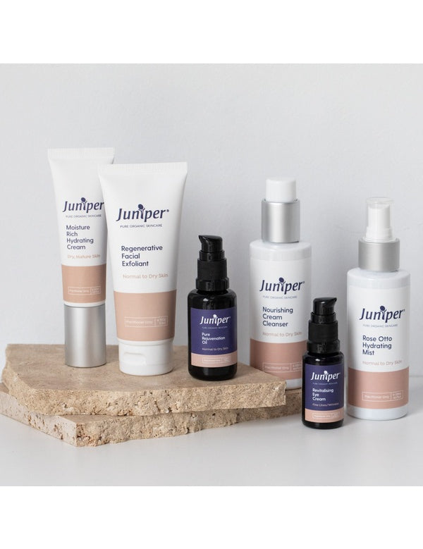 Juniper skincare range arranged on pale stone blocks, including the Nourishing Cream Cleanser, facial exfoliant, moisturiser, oils, eye cream and hydrating mist.