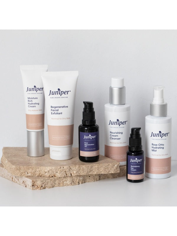 Juniper skincare range arranged on pale stone blocks, including the Nourishing Cream Cleanser, facial exfoliant, moisturiser, oils, eye cream and hydrating mist.