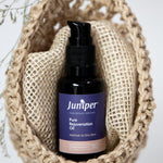Juniper Pure Rejuvenation Oil bottle styled upright inside a woven natural-fibre pouch with dried botanical details.