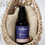 Juniper Pure Rejuvenation Oil bottle styled upright inside a woven natural-fibre pouch with dried botanical details.