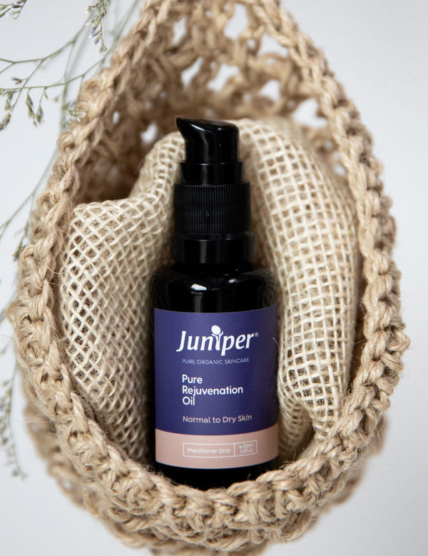 Juniper Pure Rejuvenation Oil bottle styled upright inside a woven natural-fibre pouch with dried botanical details.