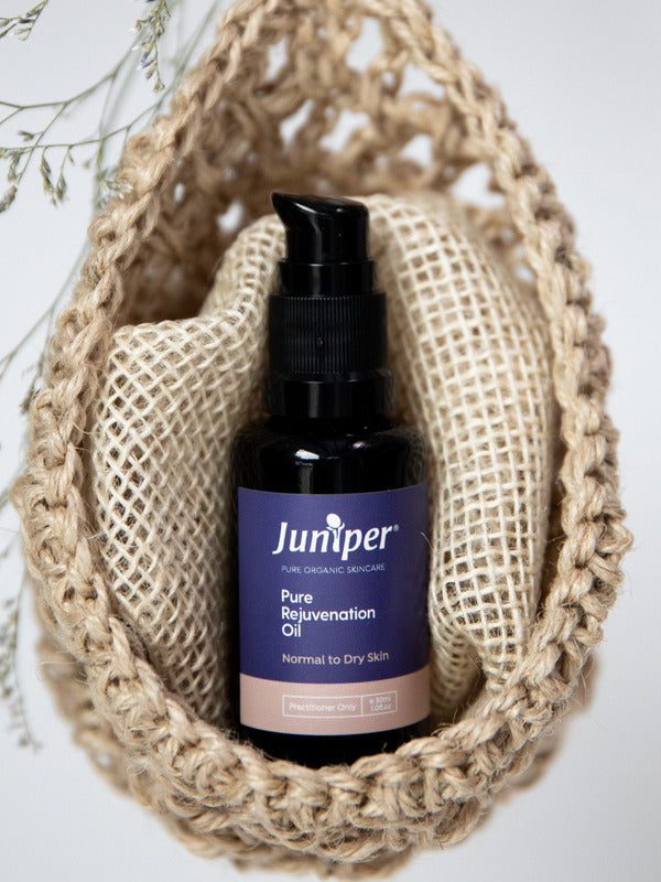 Juniper Pure Rejuvenation Oil bottle styled upright inside a woven natural-fibre pouch with dried botanical details.