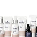 Seven Juniper skincare products arranged in a row on white: three white tubes, two tall white bottles and two small black pump bottles, with peach-coloured label bands.
