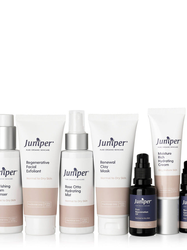 Seven Juniper skincare products arranged in a row on white: three white tubes, two tall white bottles and two small black pump bottles, with peach-coloured label bands.