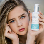 Young woman holding a bottle of Juniper Teen Cleanser beside her face.