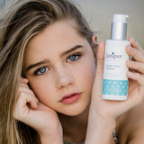 Young woman holding a bottle of Juniper Teen Cleanser beside her face.