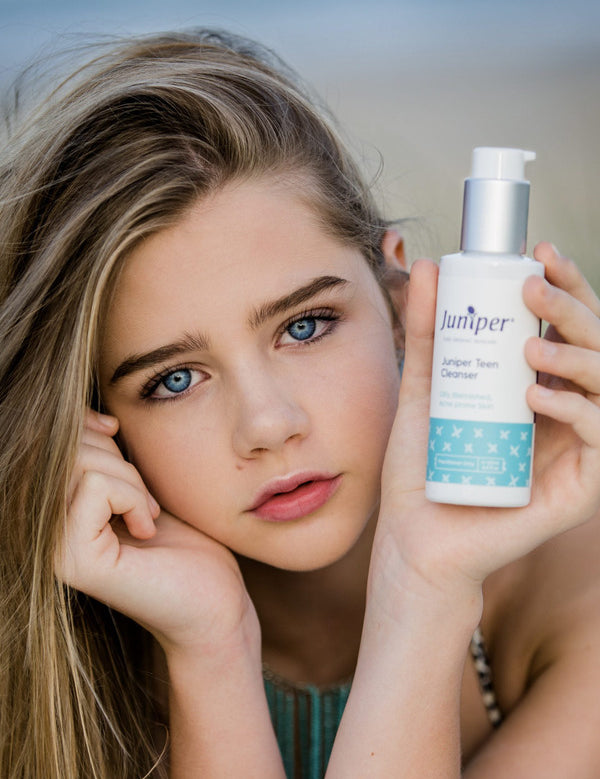 Young woman holding a bottle of Juniper Teen Cleanser beside her face.