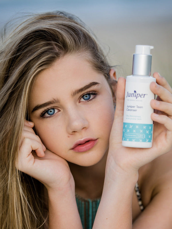 Young woman holding a bottle of Juniper Teen Cleanser beside her face.