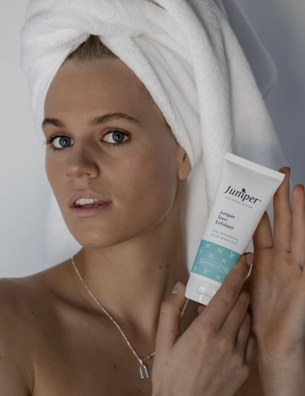 Young woman holding Juniper Teen Exfoliant beside her face.