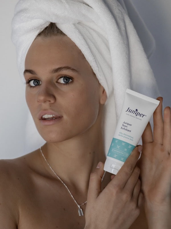 Young woman holding Juniper Teen Exfoliant beside her face.