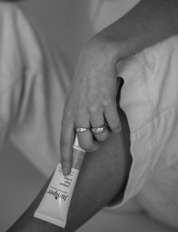 Black-and-white lifestyle image of a person holding a tube of Juniper Teen Lotion while seated.