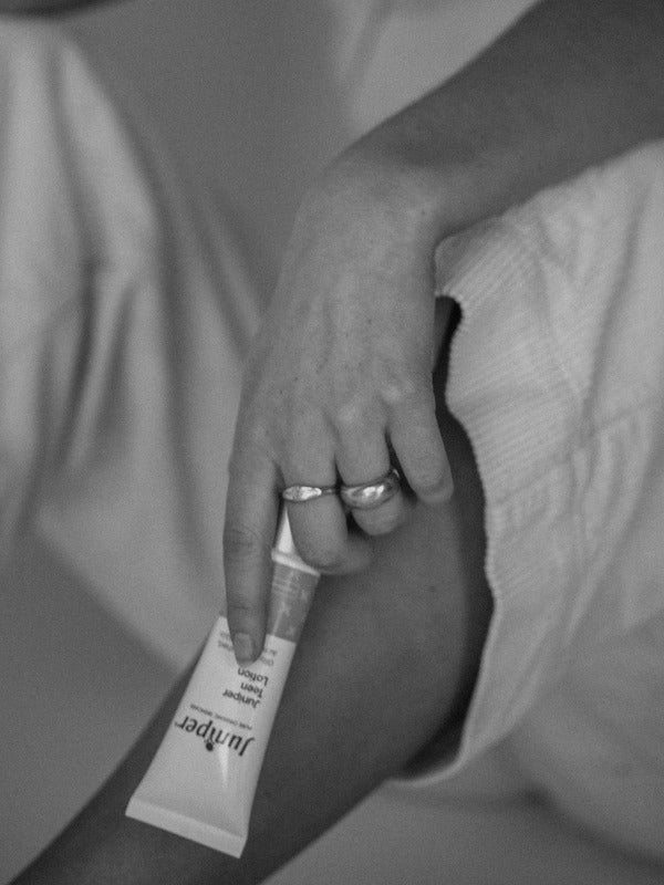 Black-and-white lifestyle image of a person holding a tube of Juniper Teen Lotion while seated.