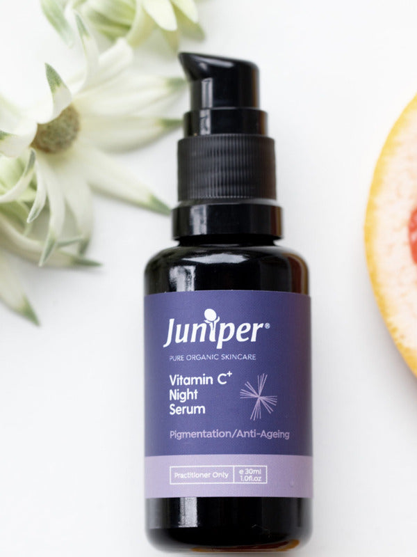 Juniper Vitamin C Night Serum bottle styled with white flowers and a fresh grapefruit slice.