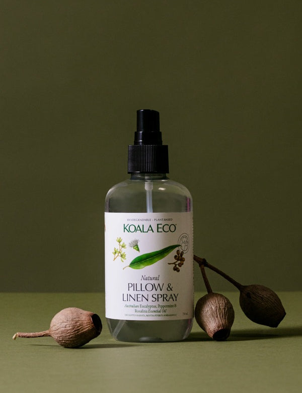 Koala Eco Pillow and Linen Spray styled with native gumnuts on a deep green background