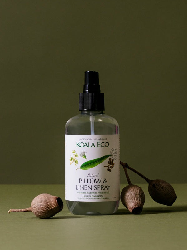 Koala Eco Pillow and Linen Spray styled with native gumnuts on a deep green background