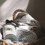 Koala Eco Pillow and Linen Spray resting in a woven laundry basket with soft blankets