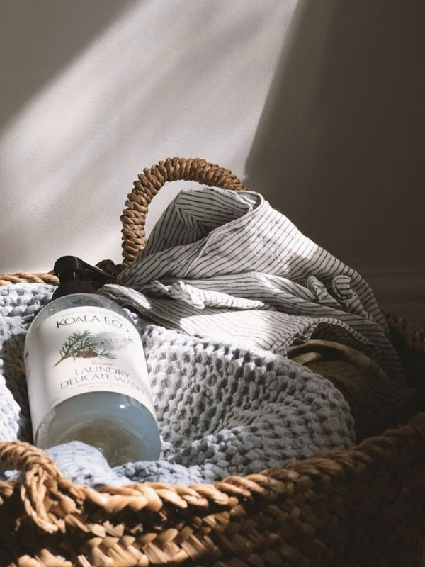 Koala Eco Pillow and Linen Spray resting in a woven laundry basket with soft blankets