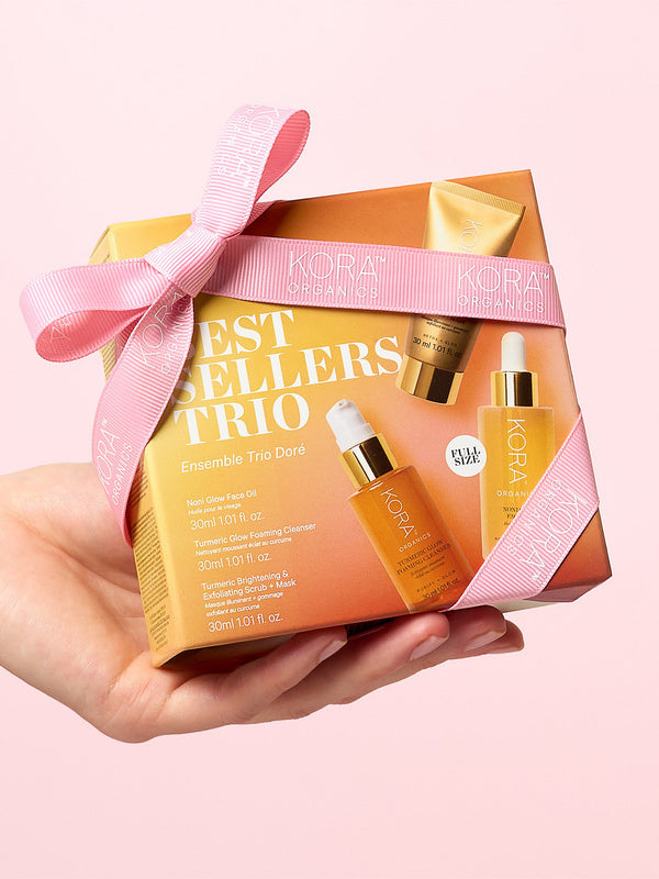KORA Organics Best Sellers Trio: Hand holding the orange gift box tied with a pink ribbon.