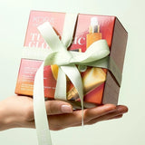 KORA Organics Turmeric Glow Trio: Hand holding the orange gift box tied with a pale green ribbon.