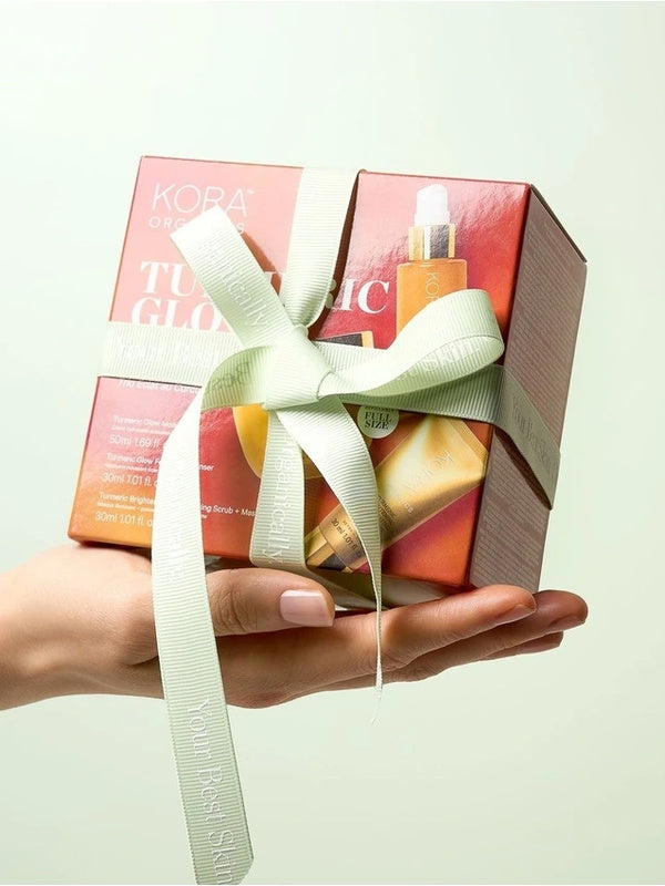 KORA Organics Turmeric Glow Trio: Hand holding the orange gift box tied with a pale green ribbon.