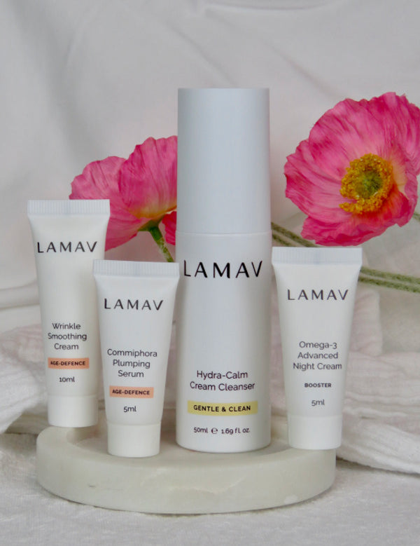 LAMAV Age-Defence Skin Discovery Pack products arranged on a tray with fresh pink flowers.