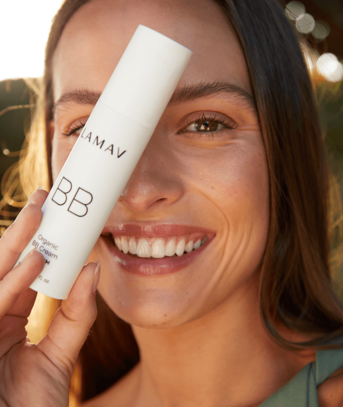 Smiling woman wearing LAMAV Organic BB Cream and holding the tube
