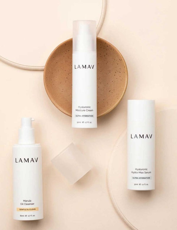 Three white LAMAV Hydration Skin Discovery products arranged around a tan ceramic dish on a soft peach background.