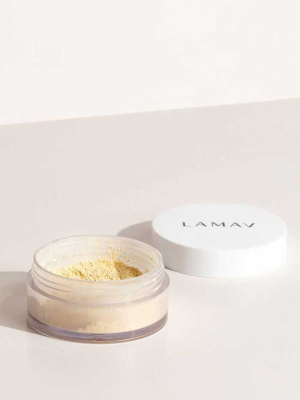 An open LAMAV Mattifying Powder 3g jar with a white lid rests on a light surface. The clear container reveals some of the yellow-tinted, talc-free powder inside.