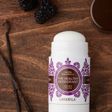 Open Lavanila Vanilla Blackberry deodorant with a rounded white stick and purple botanical label, lying on dark wood beside blackberries, vanilla pods and its brown cap.