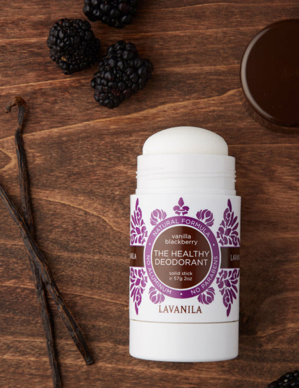 Open Lavanila Vanilla Blackberry deodorant with a rounded white stick and purple botanical label, lying on dark wood beside blackberries, vanilla pods and its brown cap.