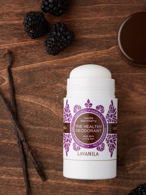 Open Lavanila Vanilla Blackberry deodorant with a rounded white stick and purple botanical label, lying on dark wood beside blackberries, vanilla pods and its brown cap.