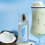 Lavanila Vanilla Coconut Hair and Body Mist arranged with fresh coconut, vanilla pods and a creamy coconut drink on blue.