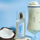 Lavanila Vanilla Coconut Hair and Body Mist arranged with fresh coconut, vanilla pods and a creamy coconut drink on blue.