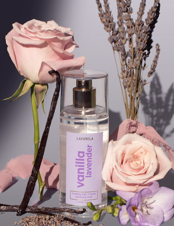 Lavanila Healthy Hair and Body Mist in Vanilla Lavender styled with pink roses, lavender stems, vanilla pods and a lilac flower.