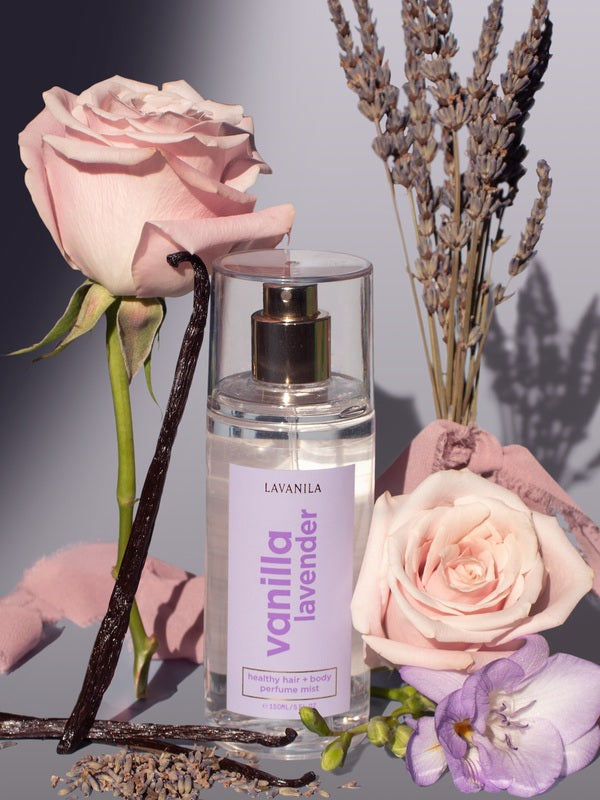 Lavanila Healthy Hair and Body Mist in Vanilla Lavender styled with pink roses, lavender stems, vanilla pods and a lilac flower.