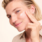 Woman smiling while applying a white streak of Lavera Basis Sensitiv Q10 Moisturising Day Cream to her cheek with one fingertip.