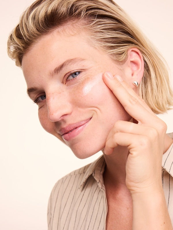 Woman smiling while applying a white streak of Lavera Basis Sensitiv Q10 Moisturising Day Cream to her cheek with one fingertip.