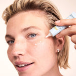 Woman applying small dots of Lavera Basis Sensitiv Q10 Anti-Ageing Eye Cream beneath her eye from the white applicator tube.