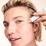 Woman applying small dots of Lavera Basis Sensitiv Q10 Anti-Ageing Eye Cream beneath her eye from the white applicator tube.
