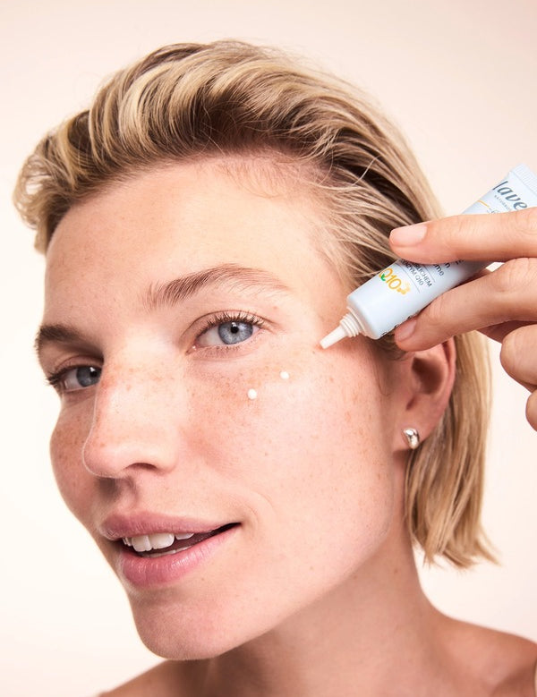 Woman applying small dots of Lavera Basis Sensitiv Q10 Anti-Ageing Eye Cream beneath her eye from the white applicator tube.