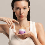 Woman holding a jar of Lavera Firming Day Cream while touching the cream with one fingertip.