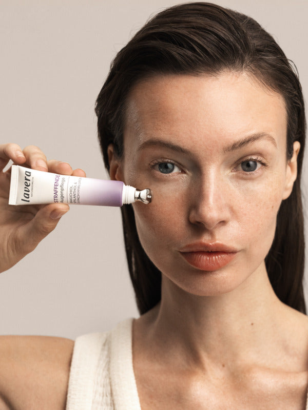 Model applying Lavera Firming Eye Cream beneath one eye from the product tube.