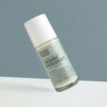Clear Noosa Basics Lemon Myrtle roll-on deodorant bottle with a pale green label and white cap tilted diagonally against a grey-green background.