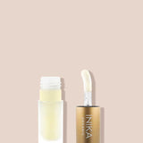 A frosted glass tube of INIKA Organic Lip Oil - Collagen + Squalane Clear with a gold cap and applicator wand is displayed on a light beige background. The cap sits beside the open tube.