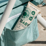 Little Urchin Baby Natural Clear Zinc Sunscreen SPF50+ 100g — the green 100g tube tucked into a striped beach bag.